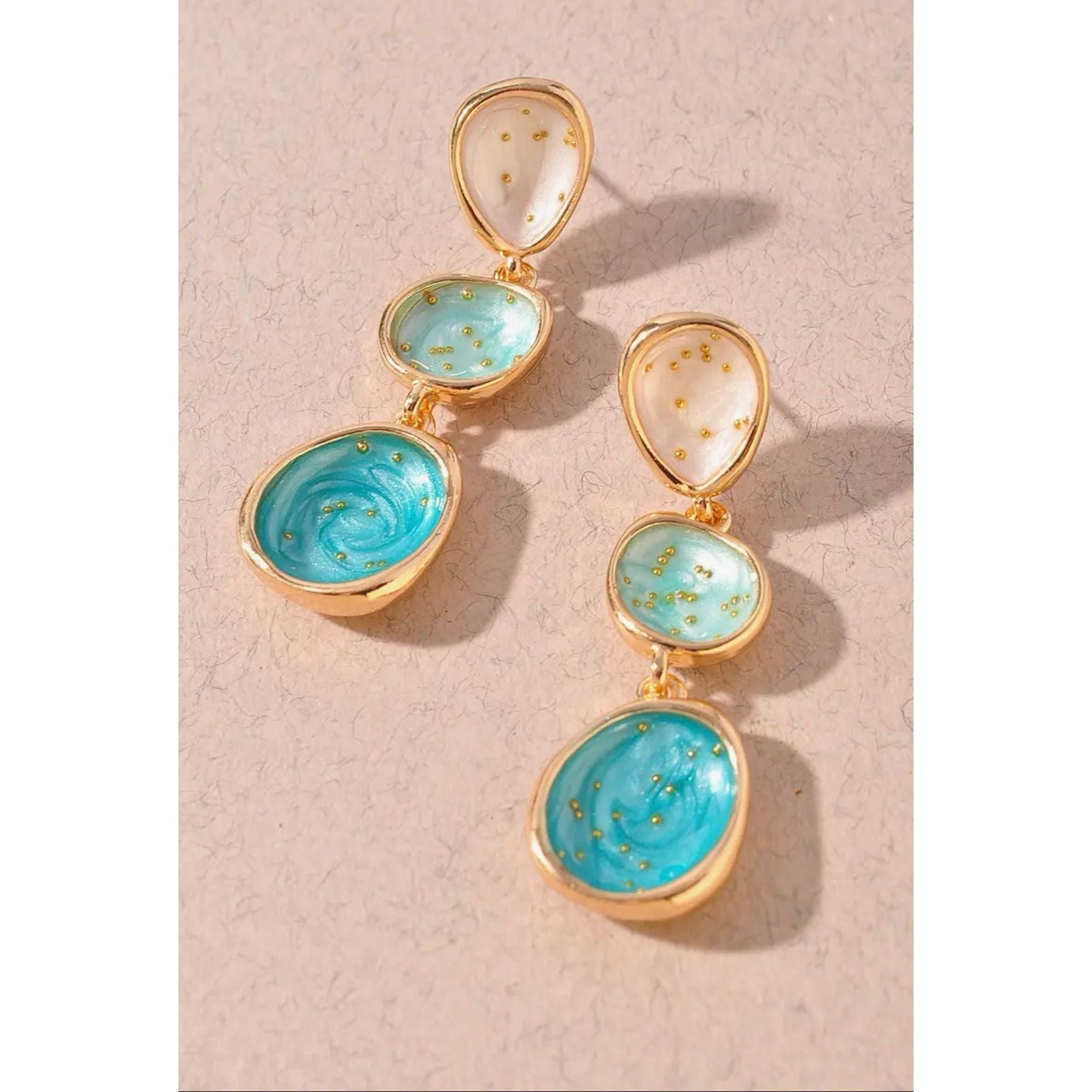 Pair of earrings with gold and turquoise stones on a beige background