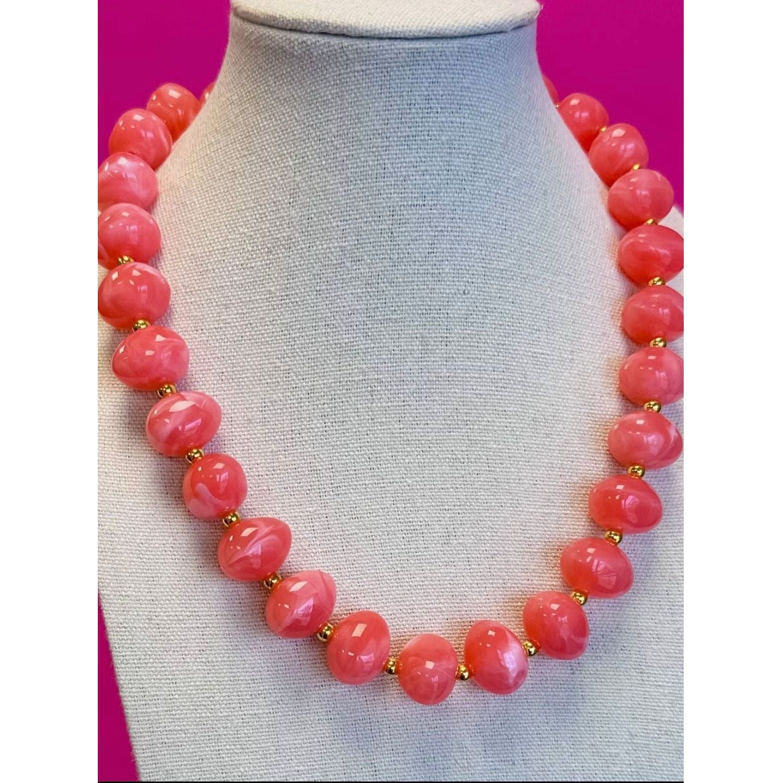 Necklace with pink beads on a mannequin against a pink background