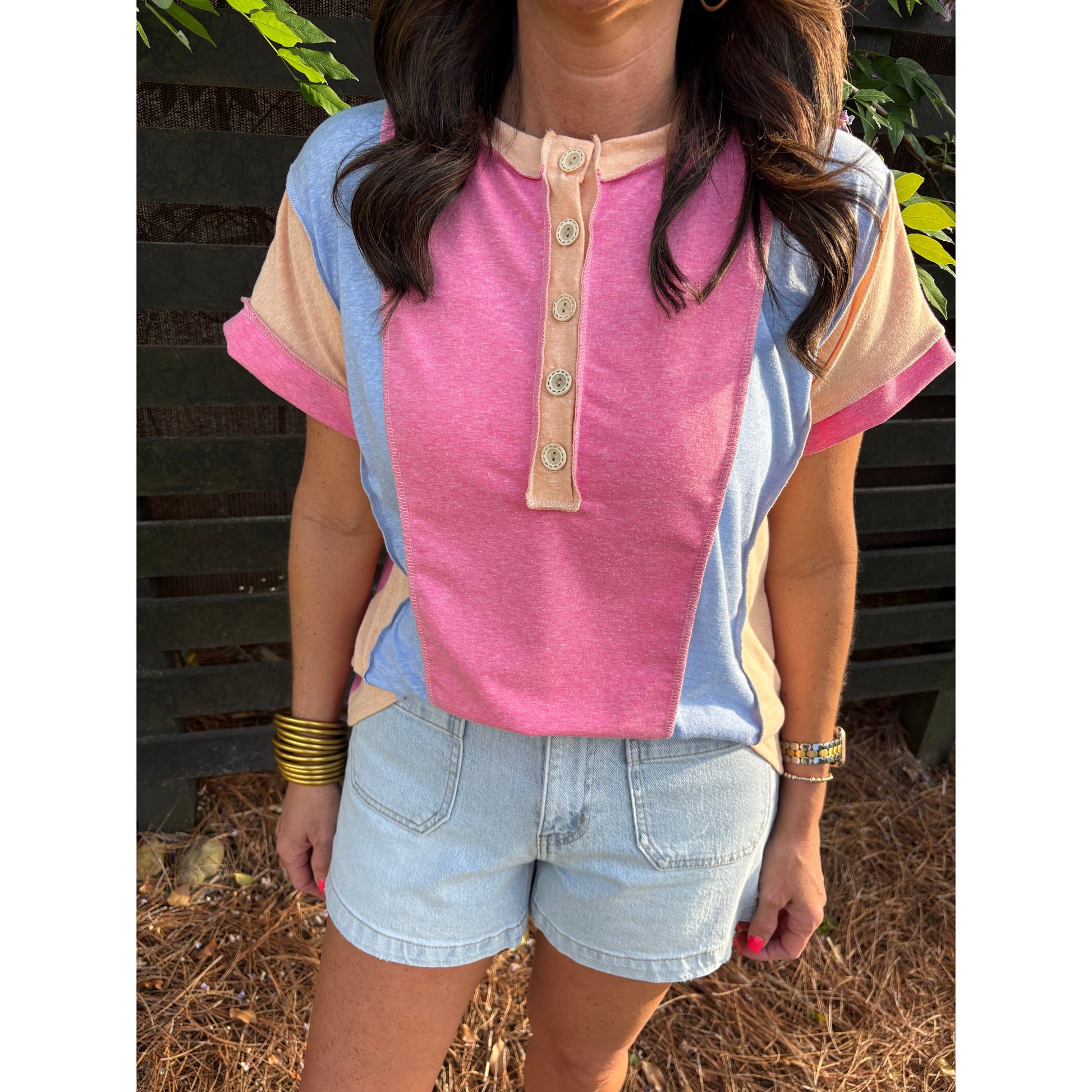 Person wearing a pink and blue shirt with denim shorts outdoors.