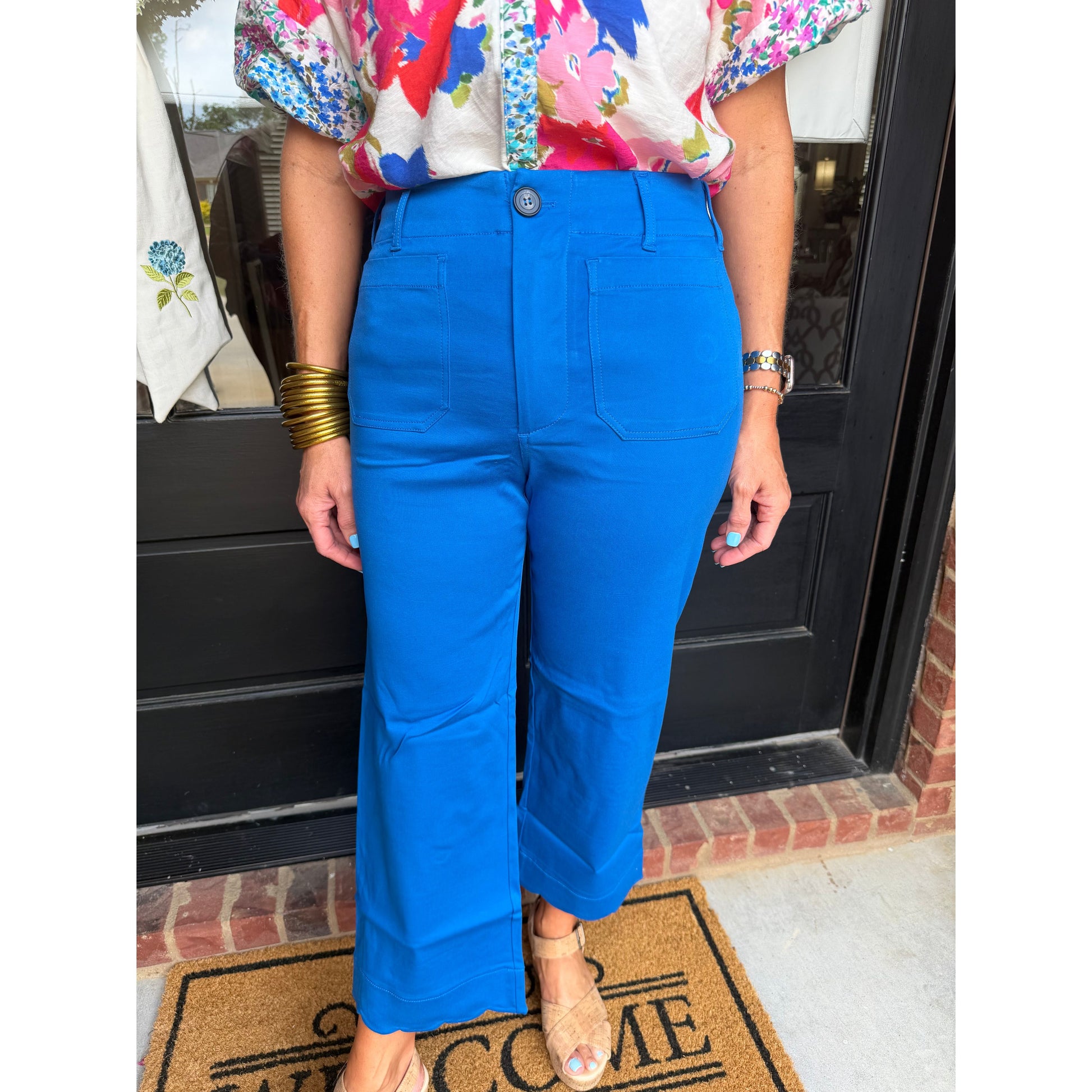 Person wearing a colorful floral blouse and blue pants standing on a doormat.