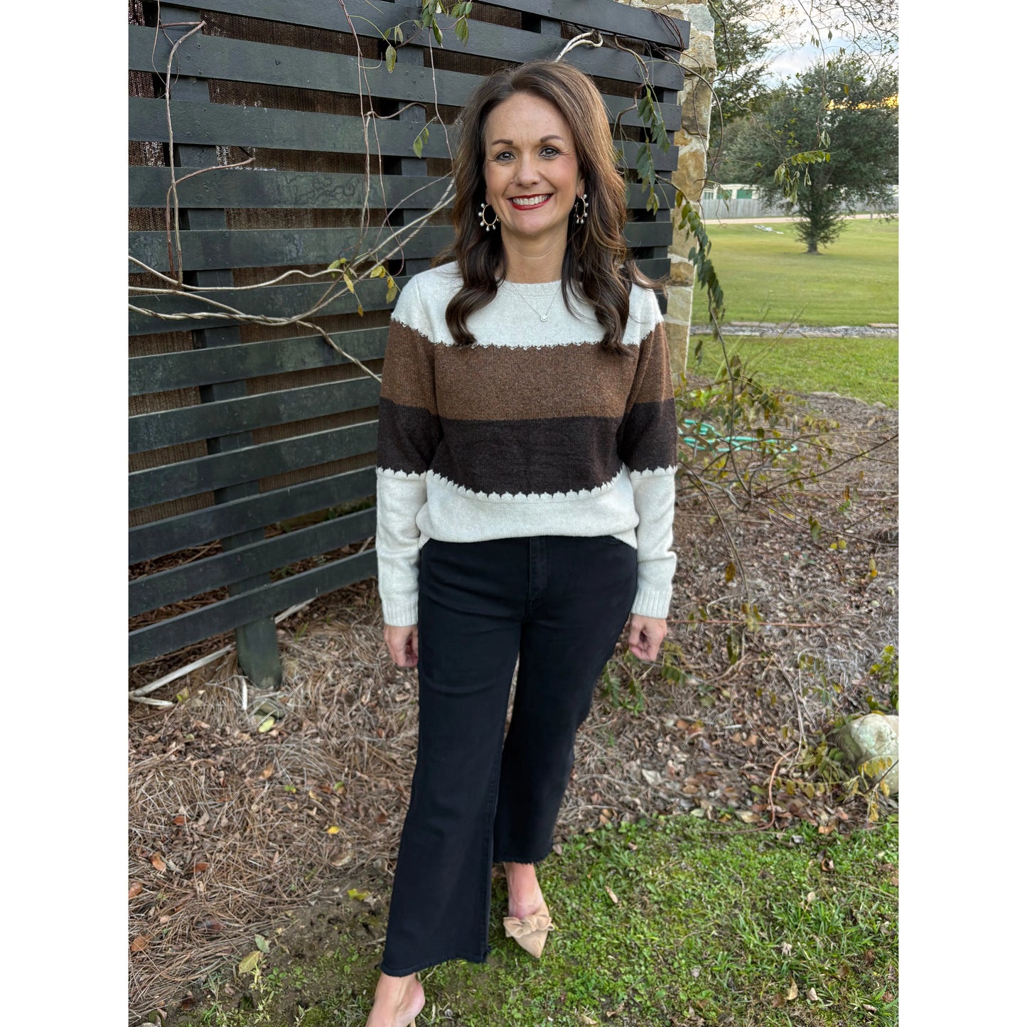 Woman wearing a striped sweater and black pants standing outdoors.
