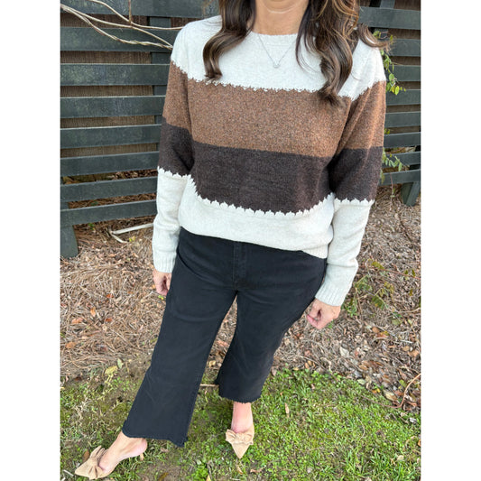 Person wearing a brown and white striped sweater with black pants outdoors.