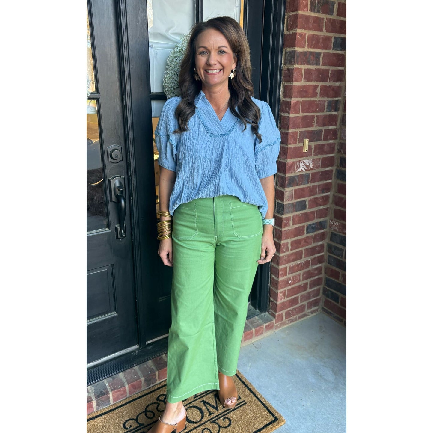 Woman in blue shirt and green pants standing outside a house.