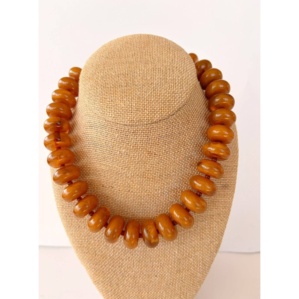 Annie Ks Boutique Rory necklace featuring large amber brown rondelle beads on a beige linen display bust