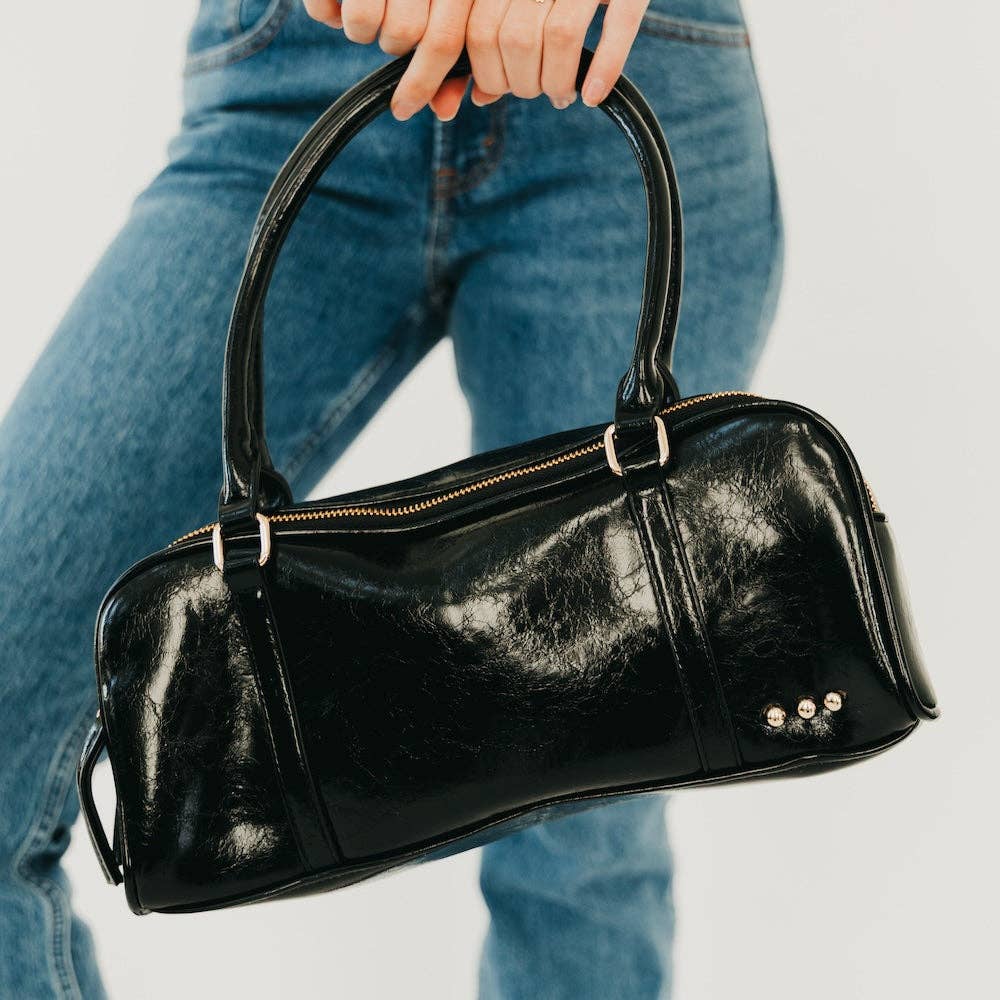 Annie Ks Boutique Arlys barrel shoulder bag in black vegan leather with top handle and gold hardware details