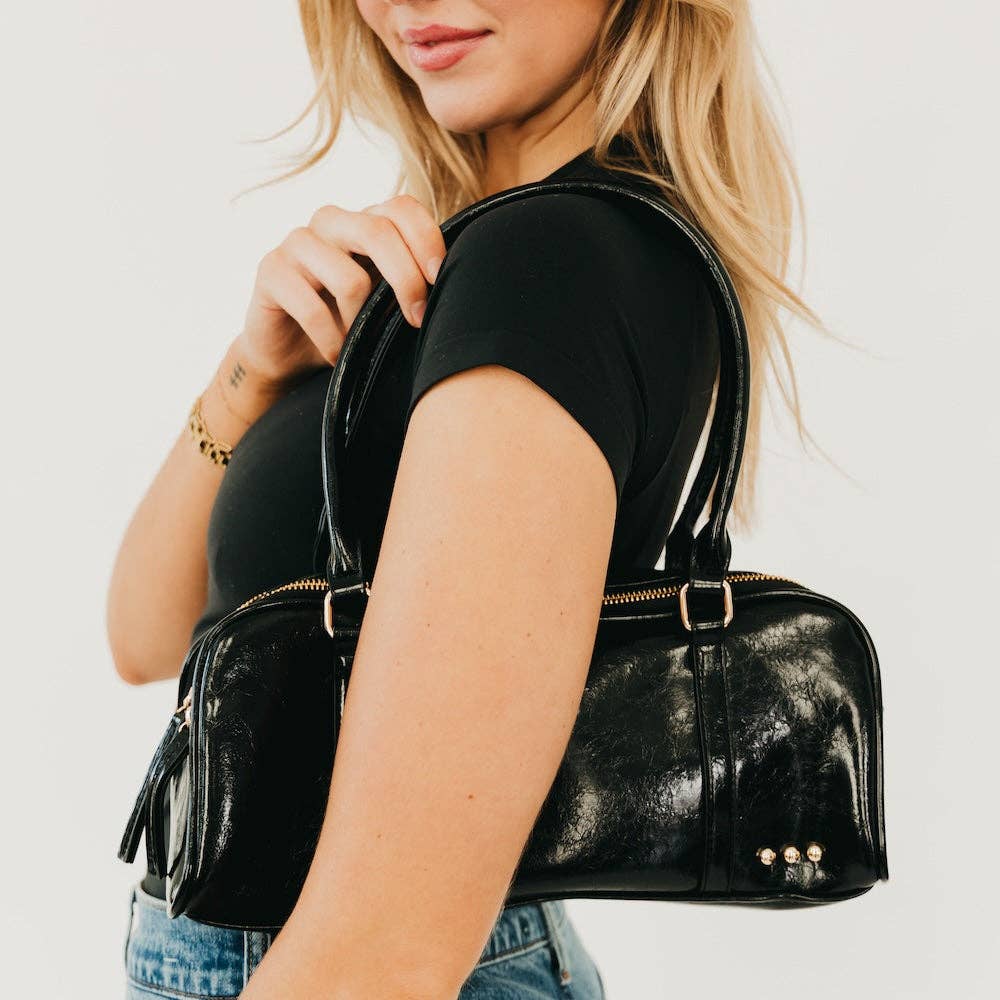 Annie Ks Boutique Arlys barrel shoulder bag in black vegan leather worn over the shoulder by a woman