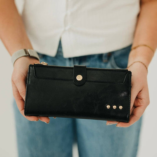 Annie Ks Boutique black Essentials Carryall Wallet held in hands, featuring gold studs and a secure snap closure.