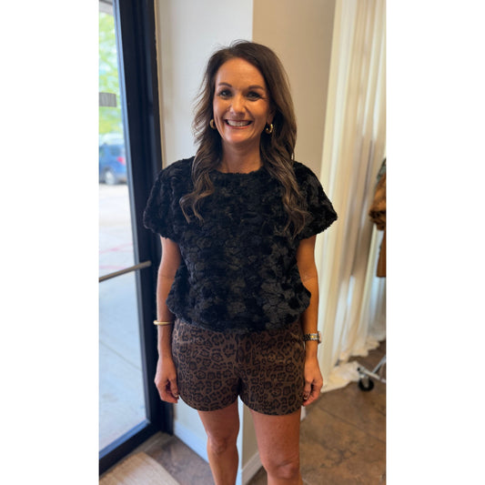 Annie Ks Boutique black plush faux-fur short sleeve top worn by a woman with brown hair in a boutique setting