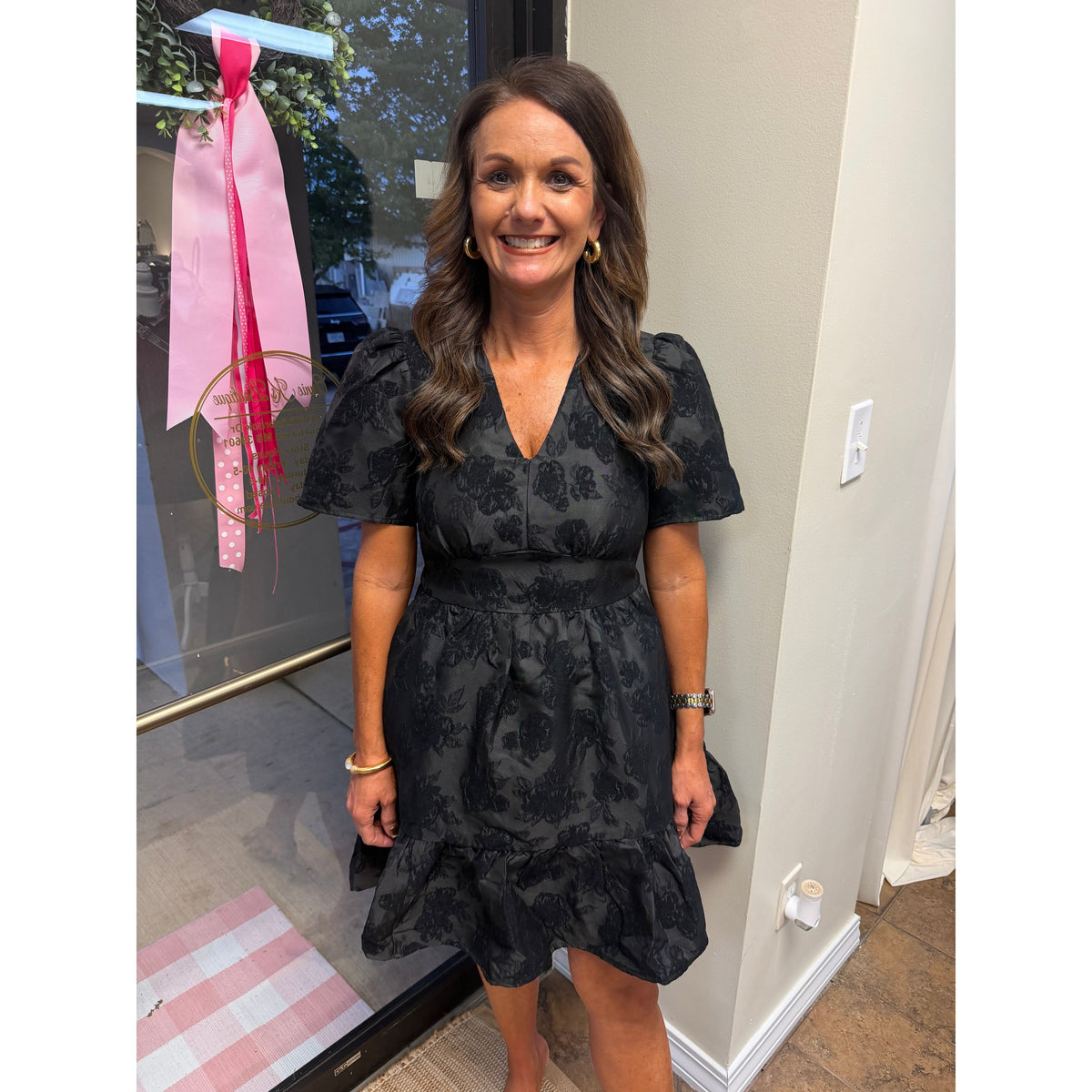 Annie Ks Boutique black jacquard mini dress with V-neck, puff sleeves, and textured floral pattern on a smiling woman