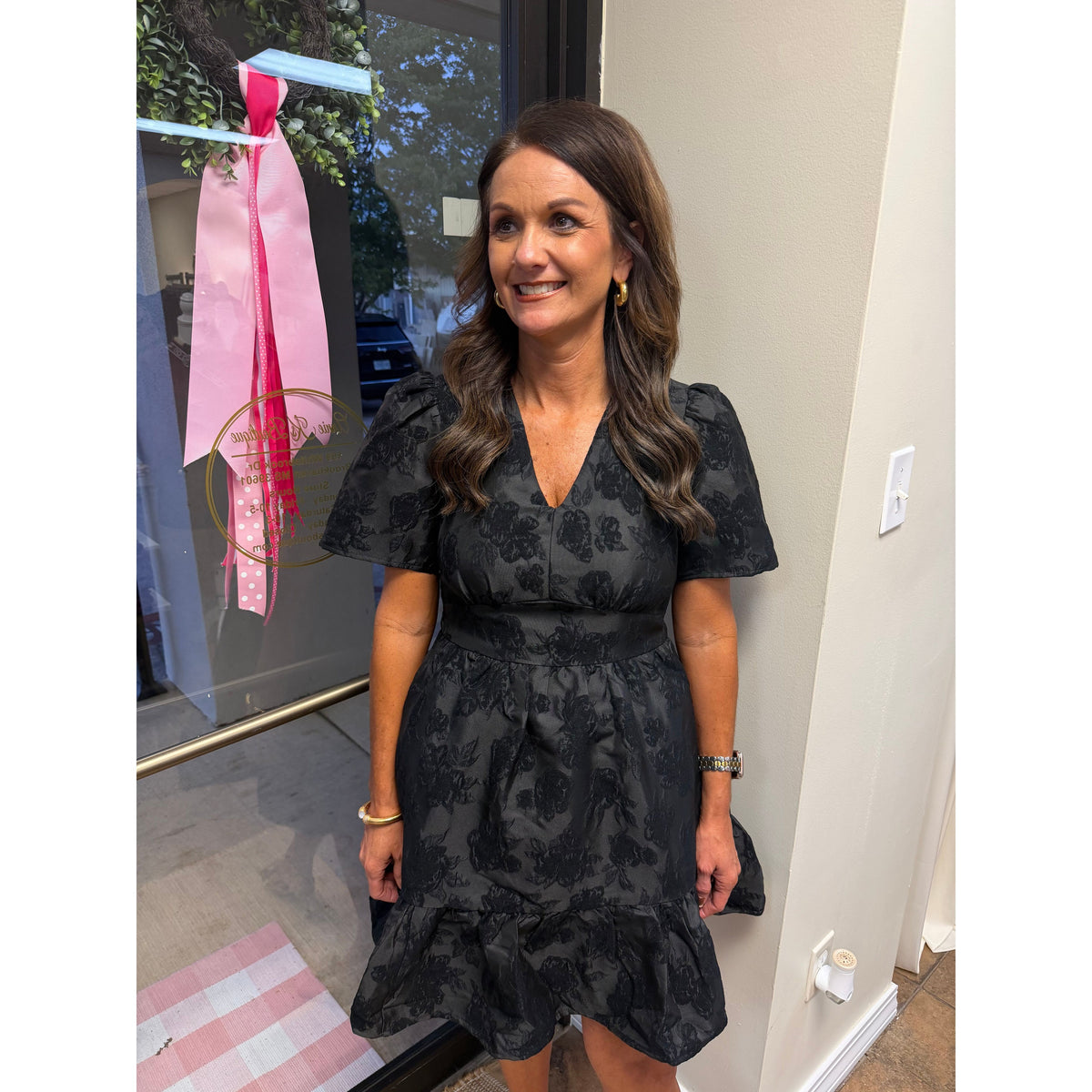 A woman wearing an Annie Ks Boutique black jacquard V-neck mini dress with textured floral patterns and patch pockets.