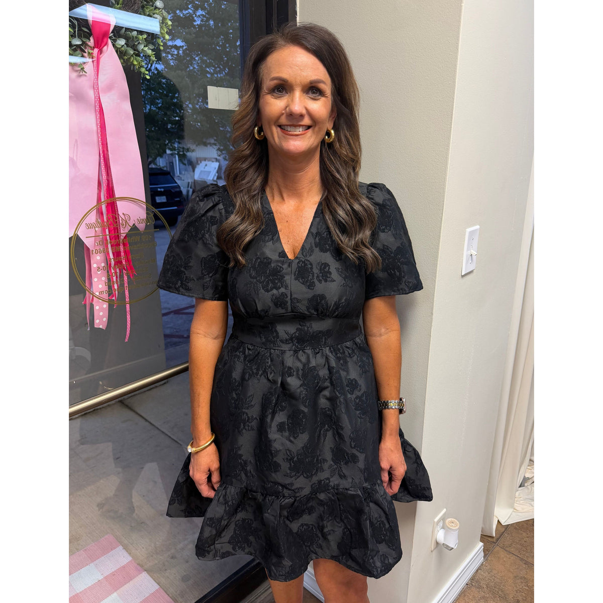 Annie Ks Boutique black jacquard mini dress with V-neck, puff sleeves, and a cinched waist on a smiling woman