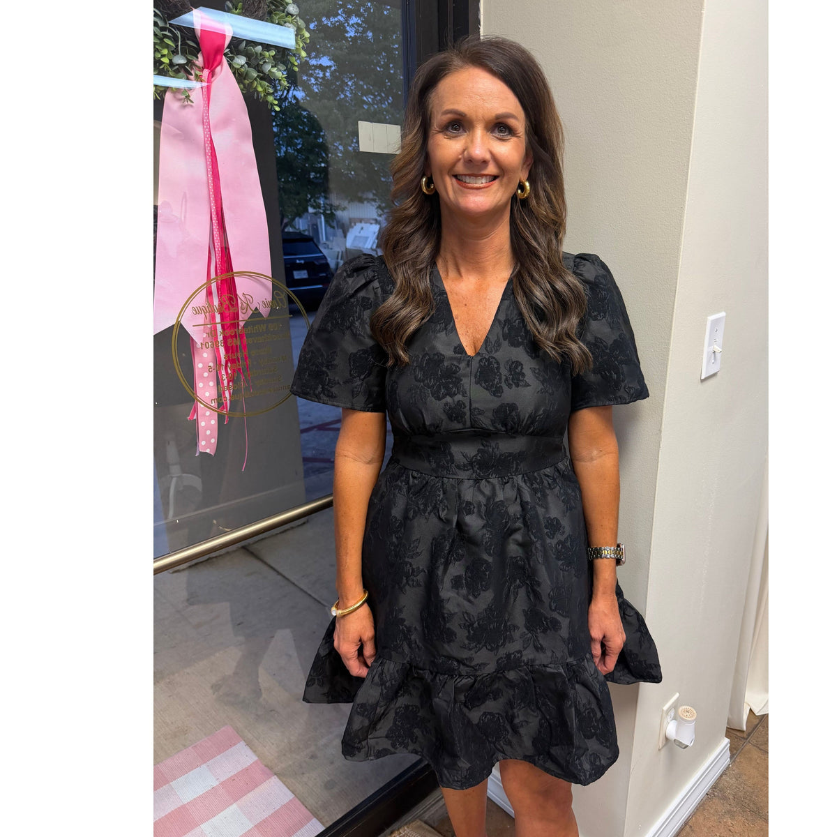 Annie Ks Boutique black jacquard mini dress with V-neck, puff sleeves, and a tiered skirt on a smiling woman