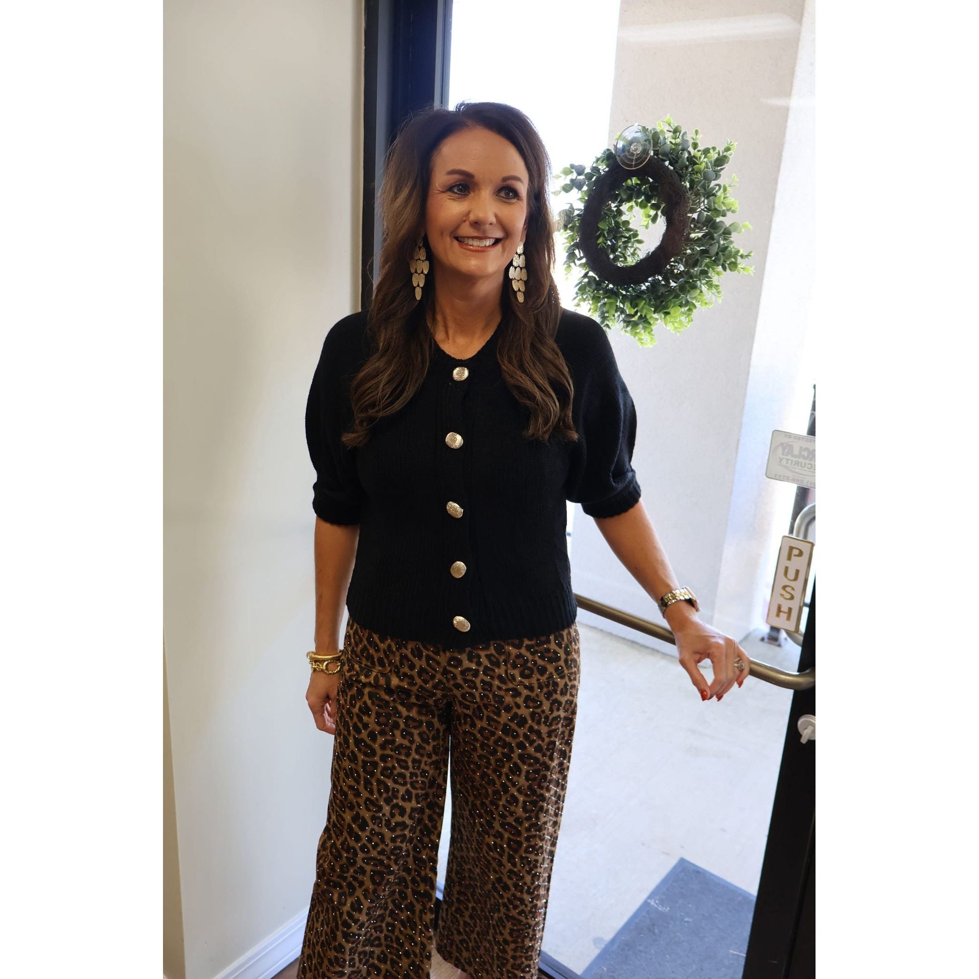 Annie Ks Boutique black knit cardigan with puff sleeves and gold buttons worn by a woman with leopard print pants