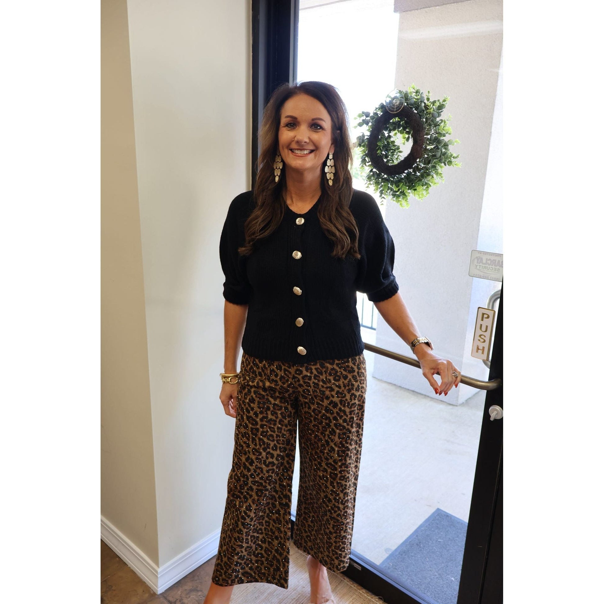 Annie Ks Boutique black puff sleeve knit cardigan with gold buttons worn by a smiling woman in leopard print pants