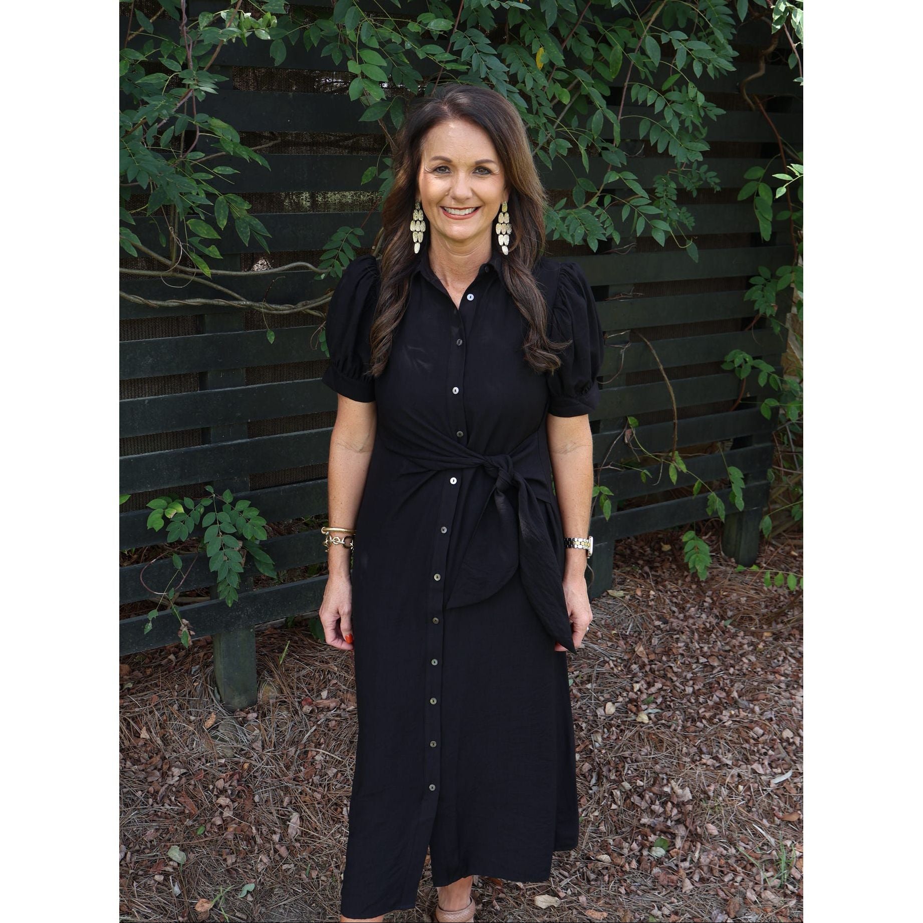 Annie Ks Boutique black midi dress with shirt collar, puff sleeves, and tie waist worn by a smiling woman outdoors.