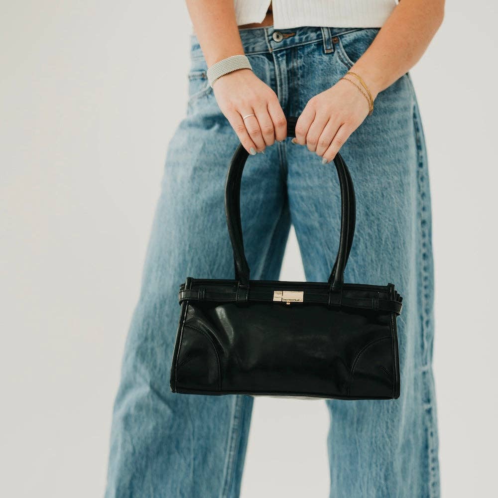 Annie Ks Boutique Ethel black vegan leather shoulder bag with gold hardware held by a person in blue jeans
