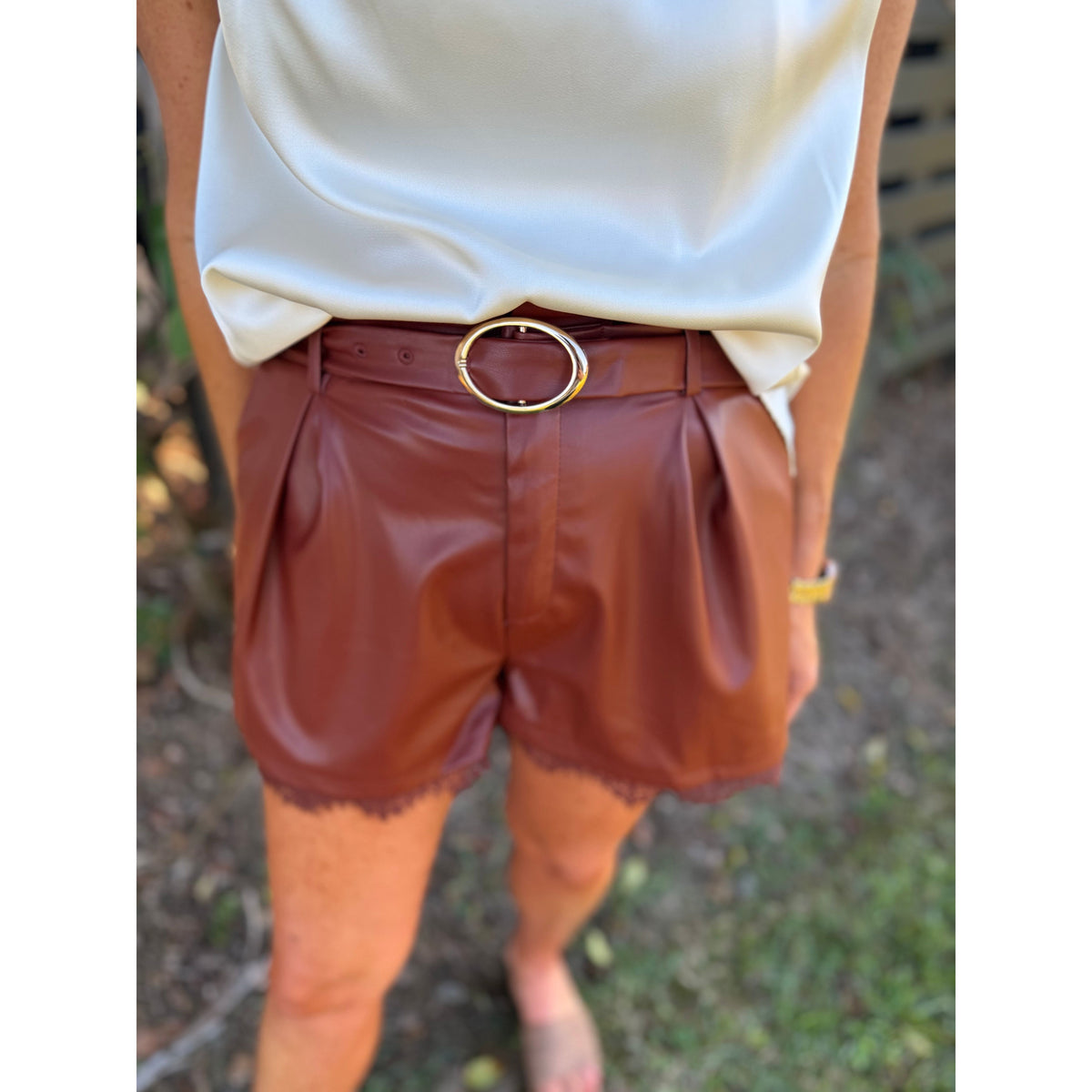 Annie Ks Boutique brick faux leather pleated shorts with delicate lace hem and gold buckle belt worn with white top