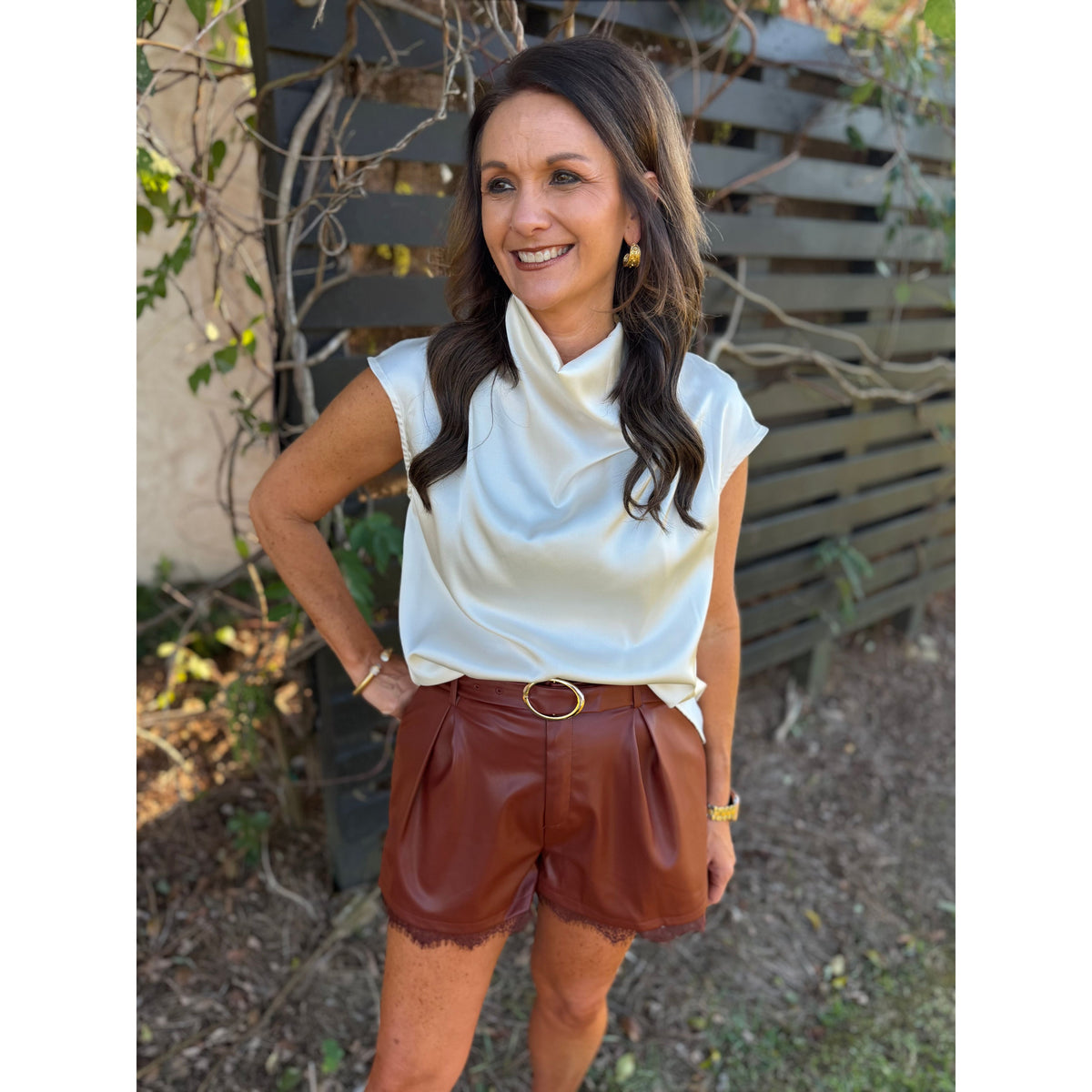 Annie Ks Boutique brick faux leather pleated shorts with a delicate lace hem and matching belt on a smiling woman