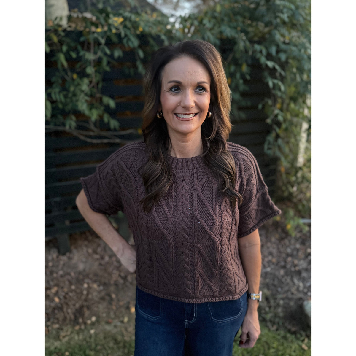 Annie Ks Boutique brown short sleeve cable knit cropped sweater with a round neck worn by a smiling woman outdoors