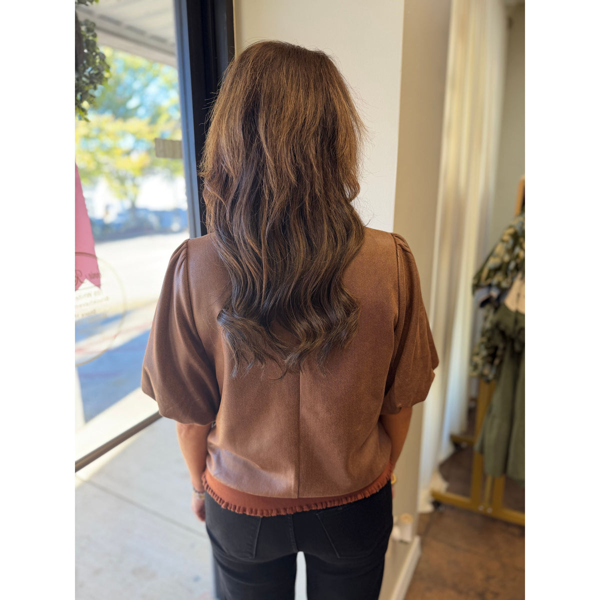 Back view of Annie Ks Boutique brown faux leather puff sleeve blouse with a banded hem worn with black jeans