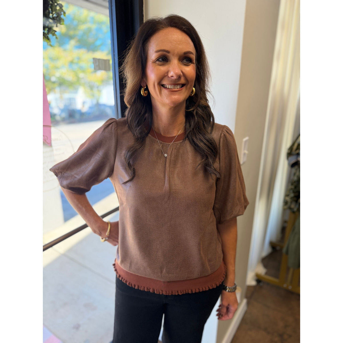 Annie Ks Boutique brown faux leather puff sleeve blouse with crew neck and banded hem worn by a smiling woman