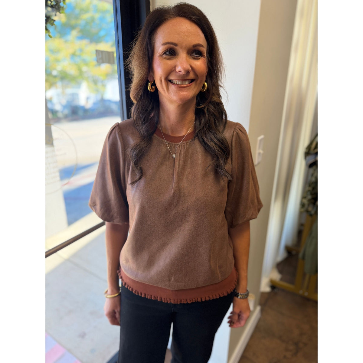 Annie Ks Boutique brown faux leather puff sleeve blouse with crew neck and banded hem worn by a smiling woman