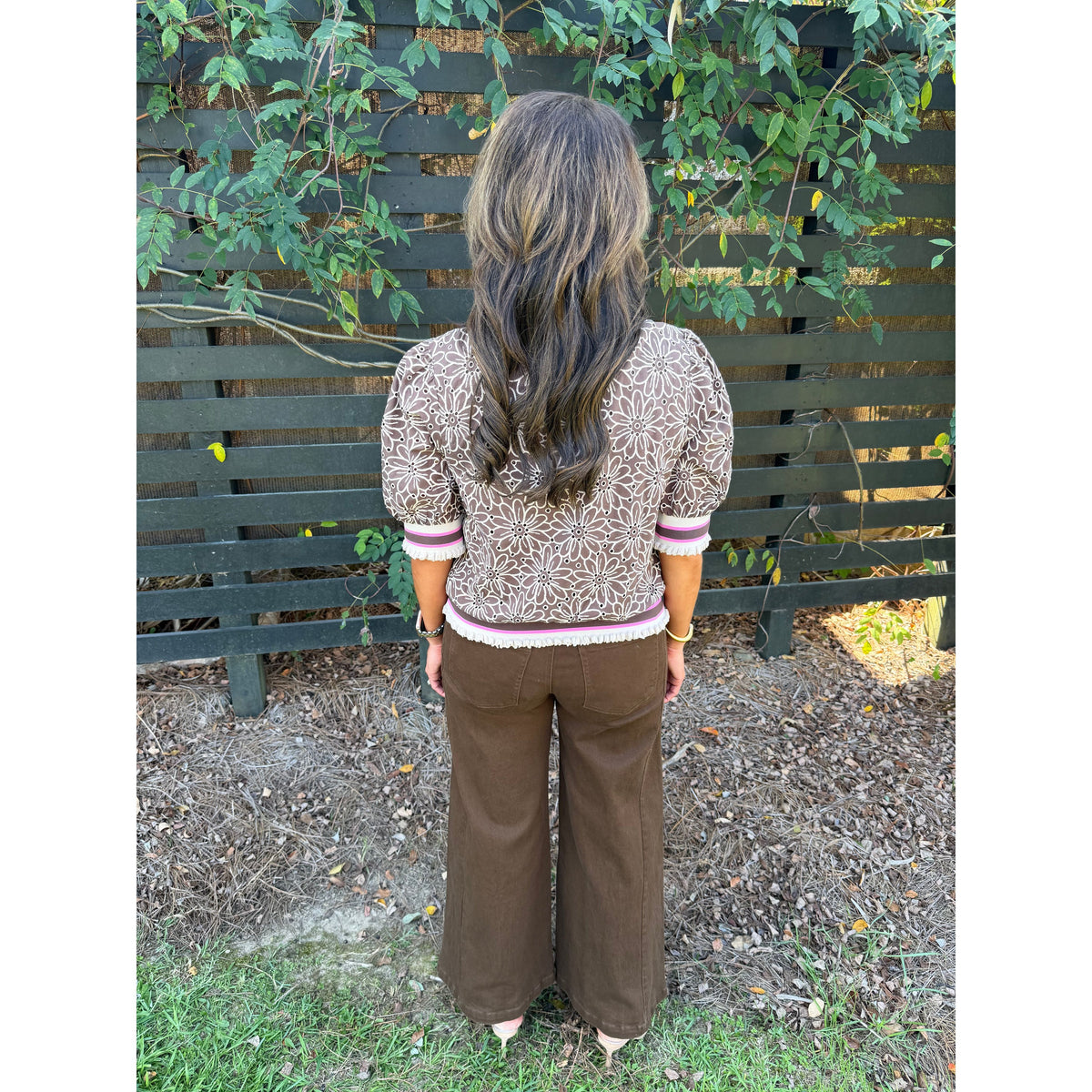 Back view of a woman wearing an Annie Ks Boutique brown floral eyelet top with puff sleeves and striped ribbed trim.