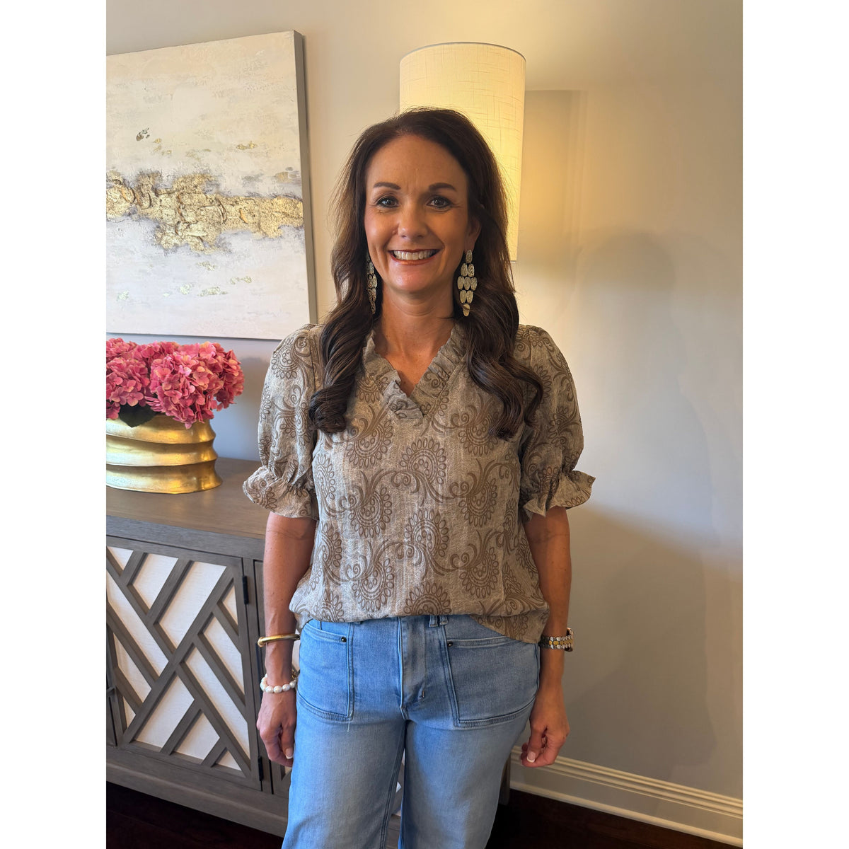 Annie Ks Boutique brown paisley print blouse with ruffle neck and puff sleeves worn by a woman with light wash jeans