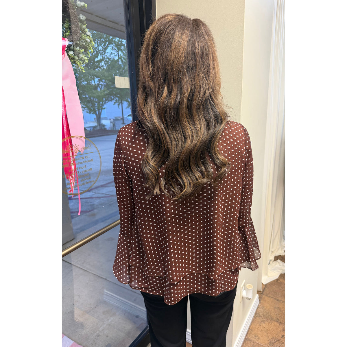 Back view of a woman wearing an Annie Ks Boutique brown polka-dot top with bell sleeves and a woven fit.