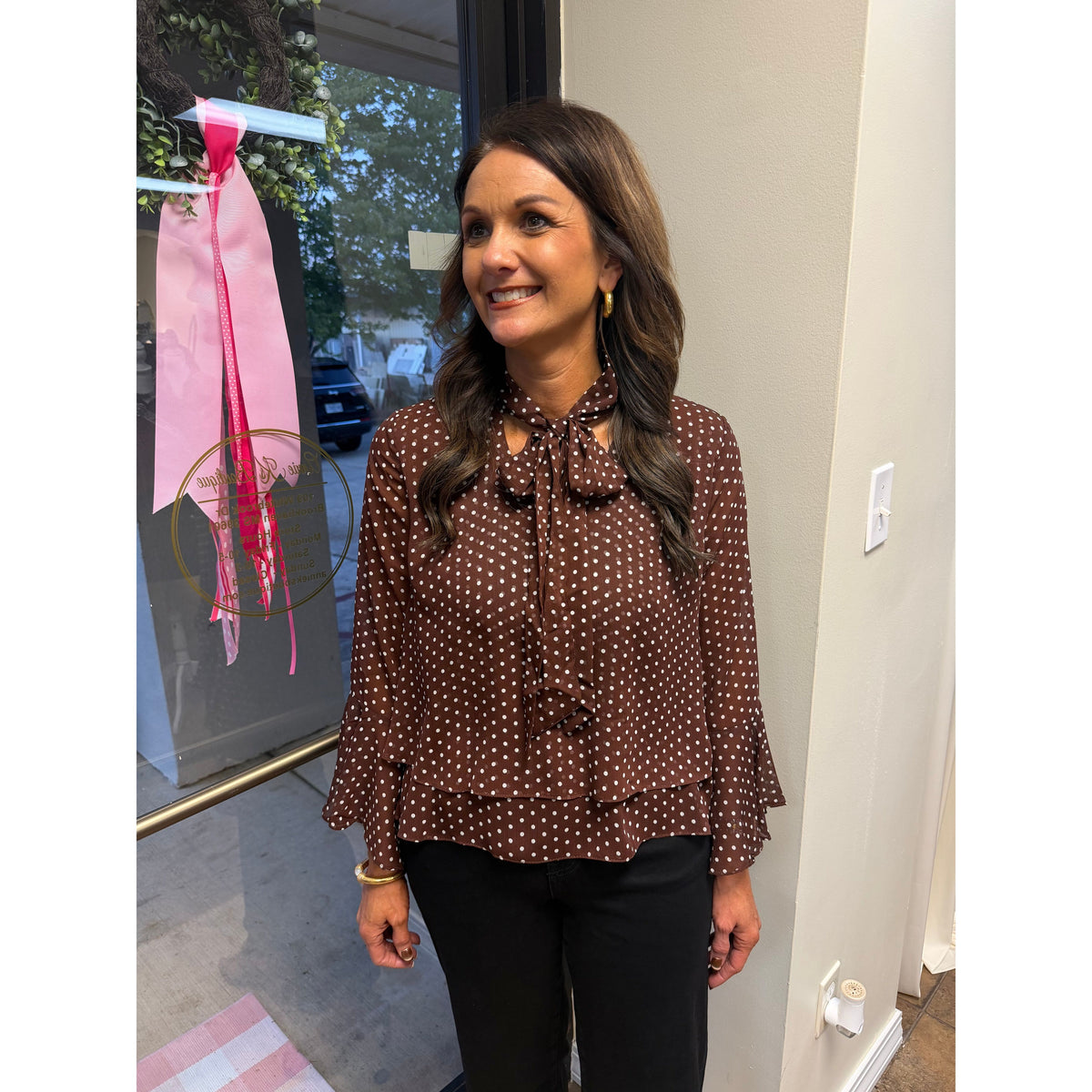 Annie Ks Boutique brown polka-dot blouse with bell sleeves and a neck bow worn by a woman in a shop