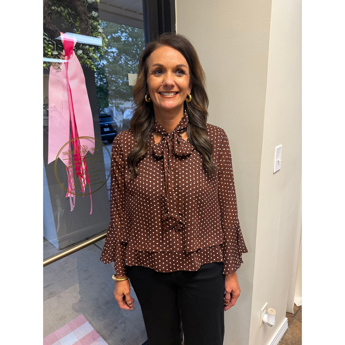 Annie Ks Boutique brown polka-dot blouse with bell sleeves and a neck bow worn by a smiling woman