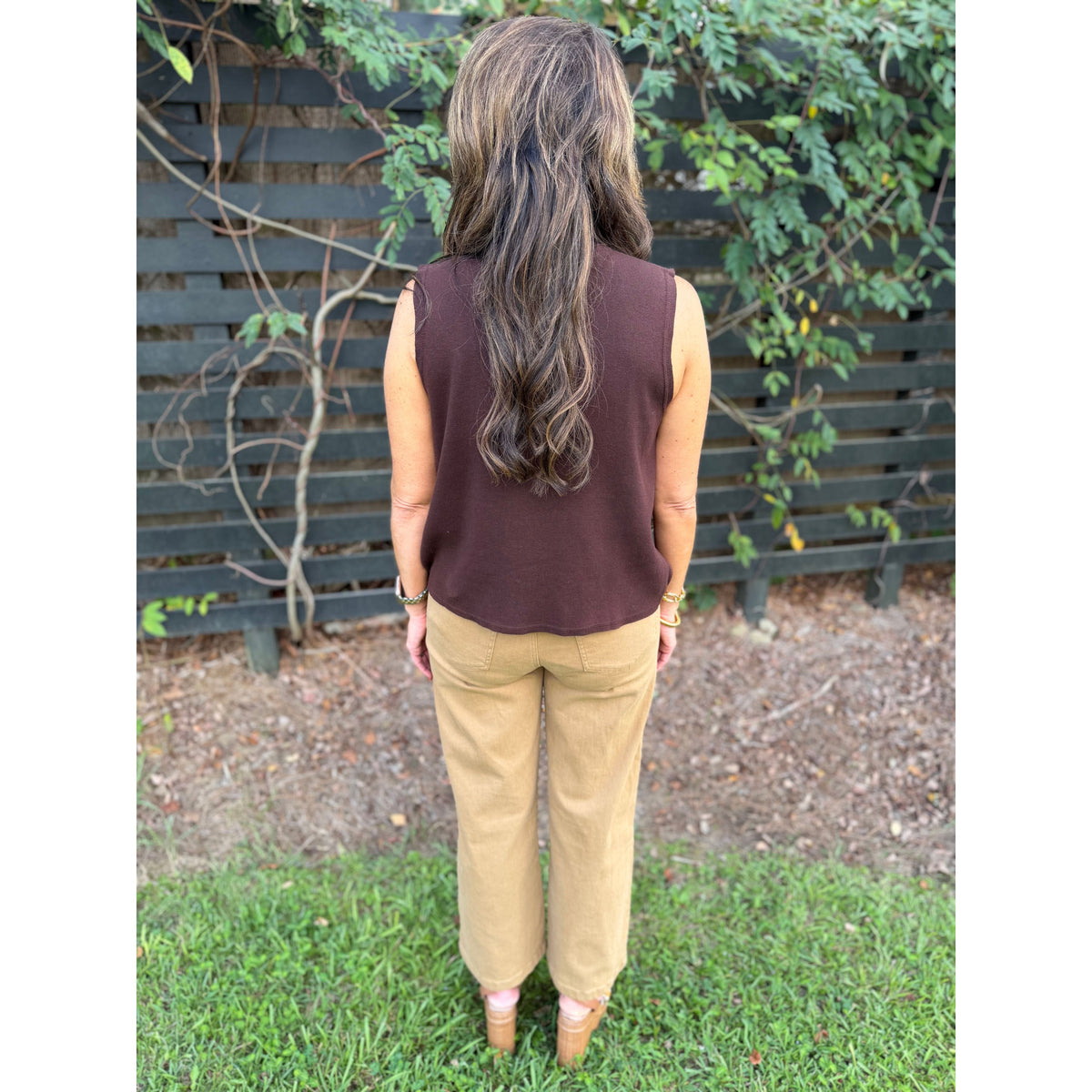 Back view of Annie Ks Boutique brown sleeveless cotton turtleneck top paired with tan trousers in a garden setting.