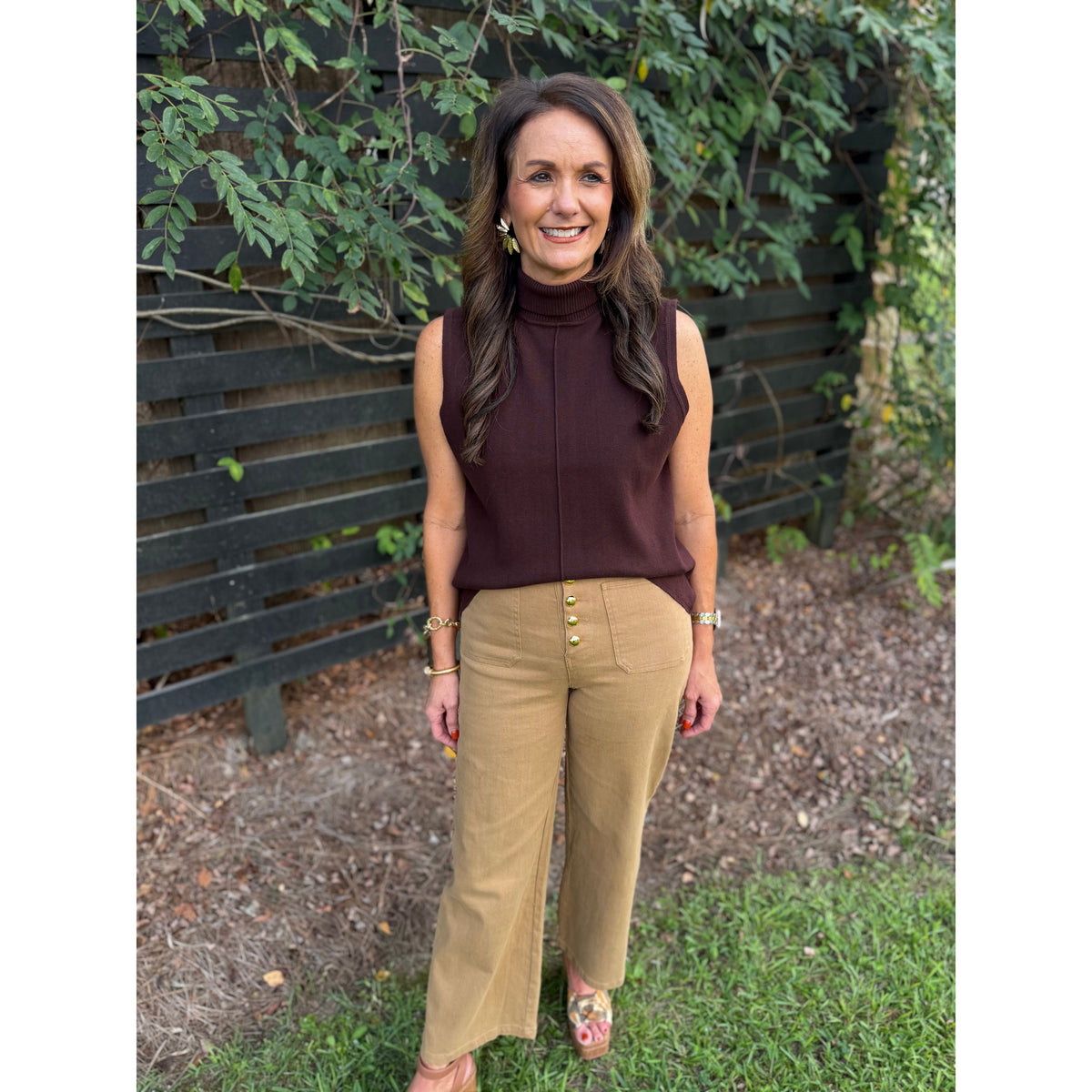 Annie Ks Boutique brown sleeveless cotton turtleneck with center-front seam worn with tan trousers in a garden setting