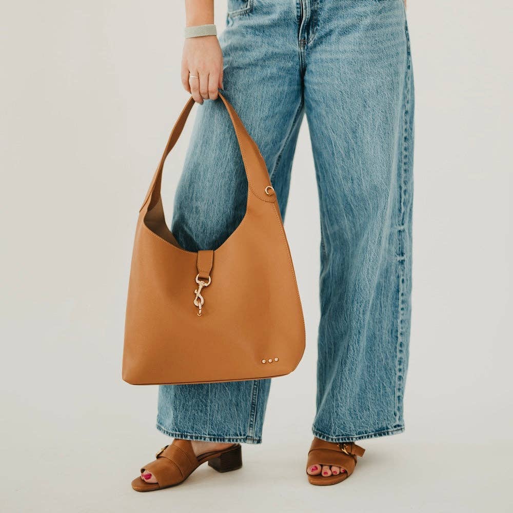 Annie Ks Boutique Haddie Hobo brown vegan leather tote bag with gold hardware lock detail held by a person in jeans