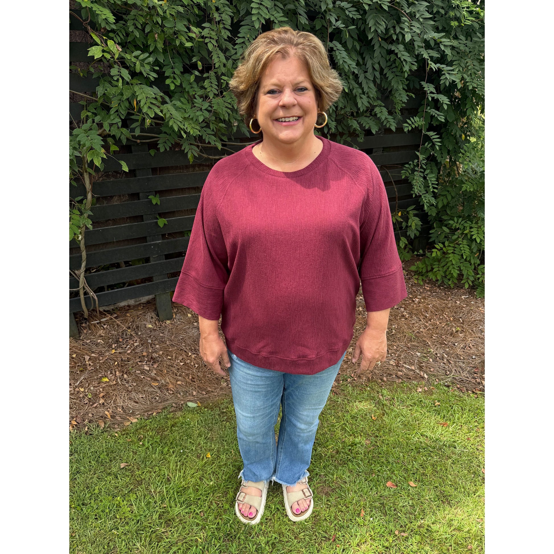 Annie Ks Boutique burgundy relaxed dolman sleeve knit sweater worn by a smiling woman with light wash denim jeans