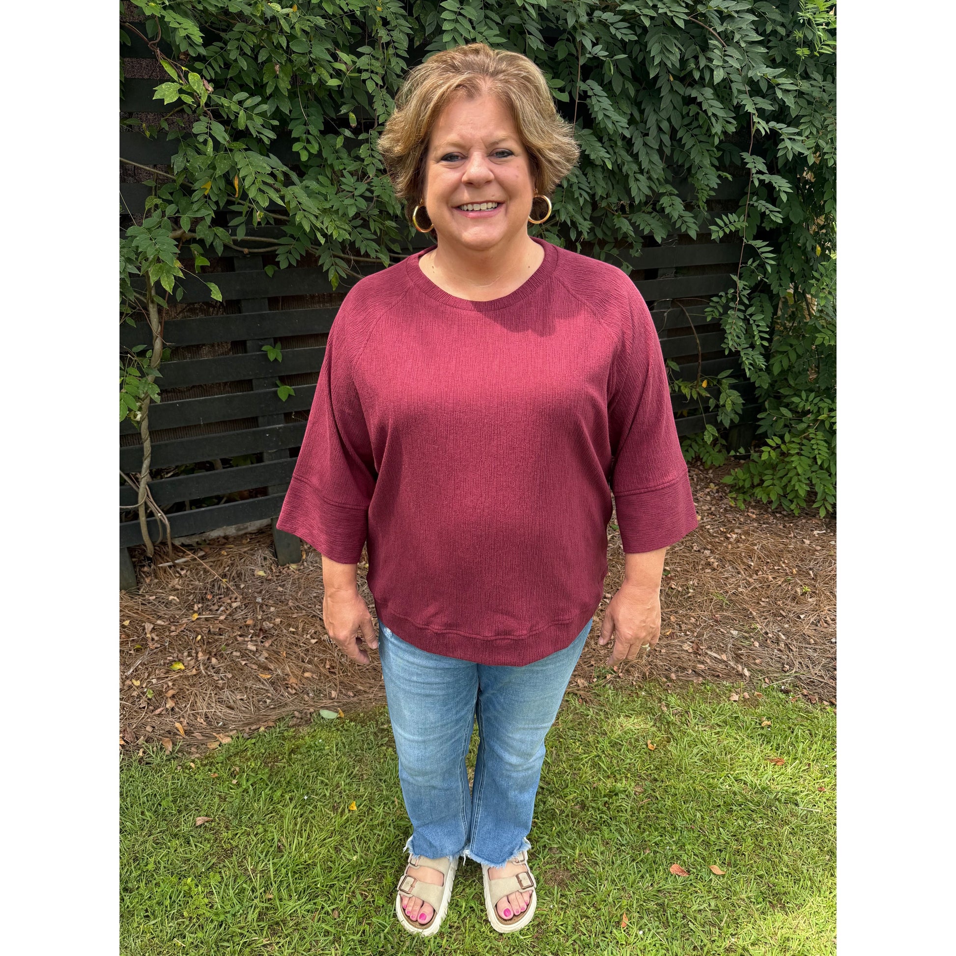 Annie Ks Boutique burgundy relaxed dolman sleeve knit sweater worn with light wash jeans and sandals outdoors