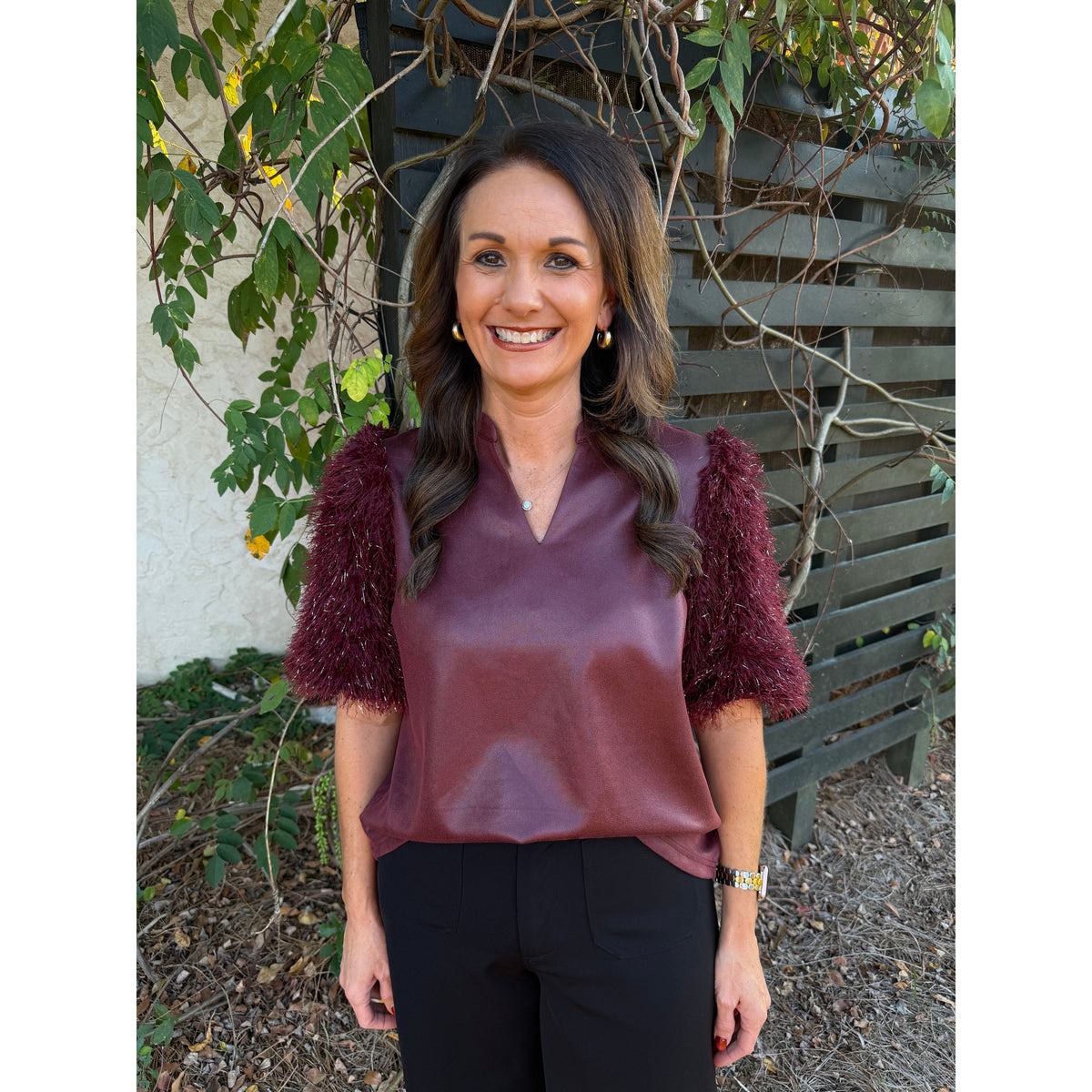 Annie Ks Boutique burgundy faux leather top with metallic feather fringe sleeves and a split neckline on a woman.
