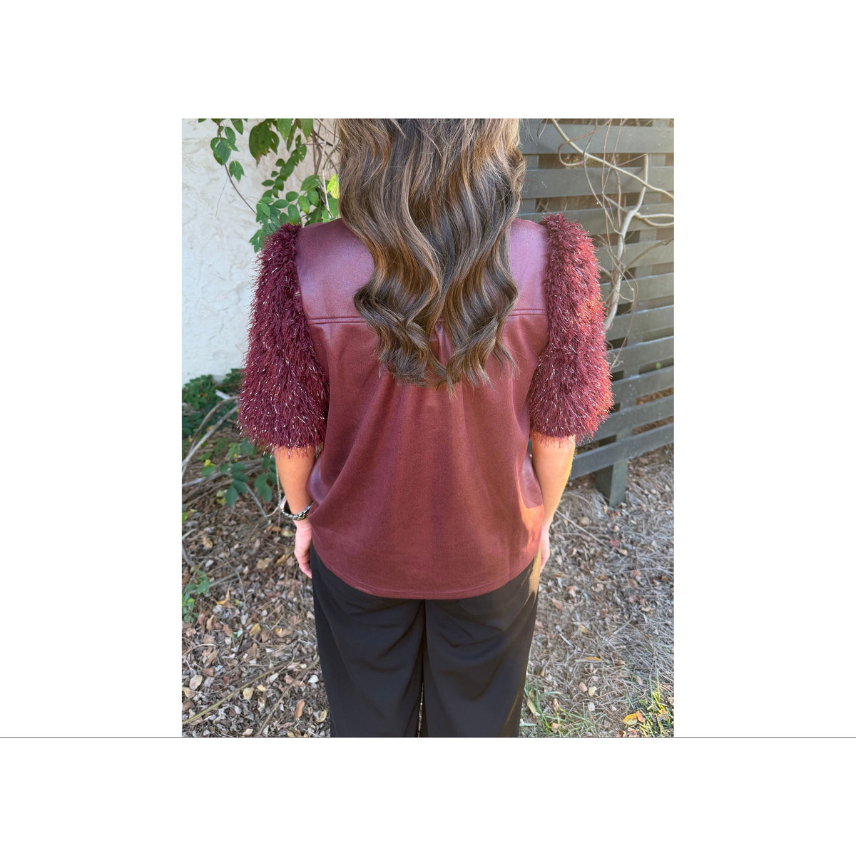 Back view of Annie Ks Boutique burgundy faux leather top with metallic feather fringe sleeves on a woman outdoors.