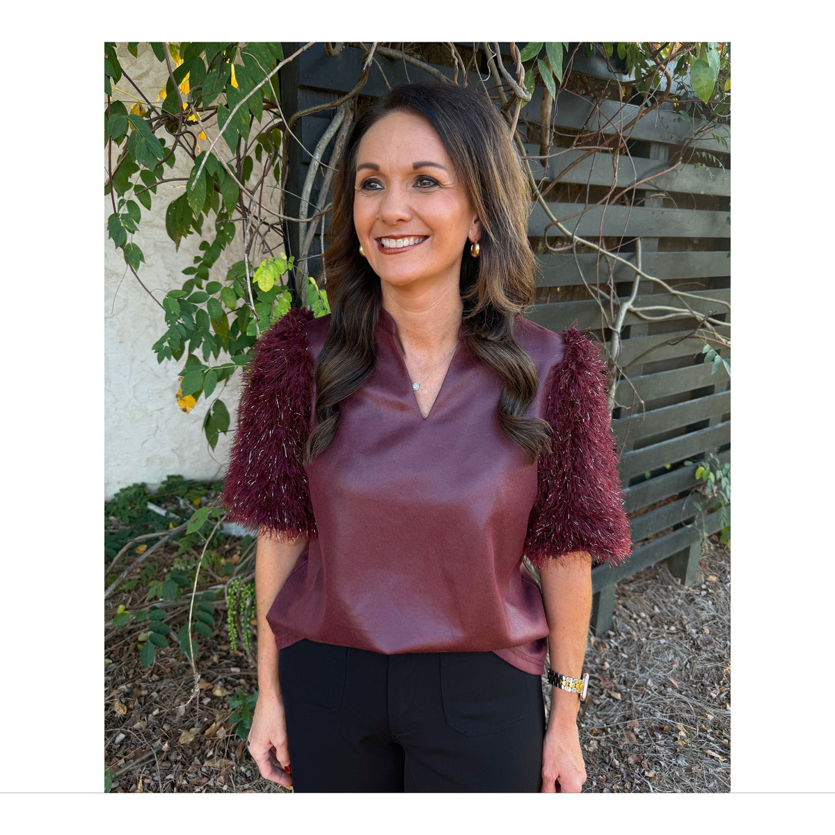 Annie Ks Boutique burgundy faux leather top with metallic feather fringe sleeves and a split neckline worn by a woman