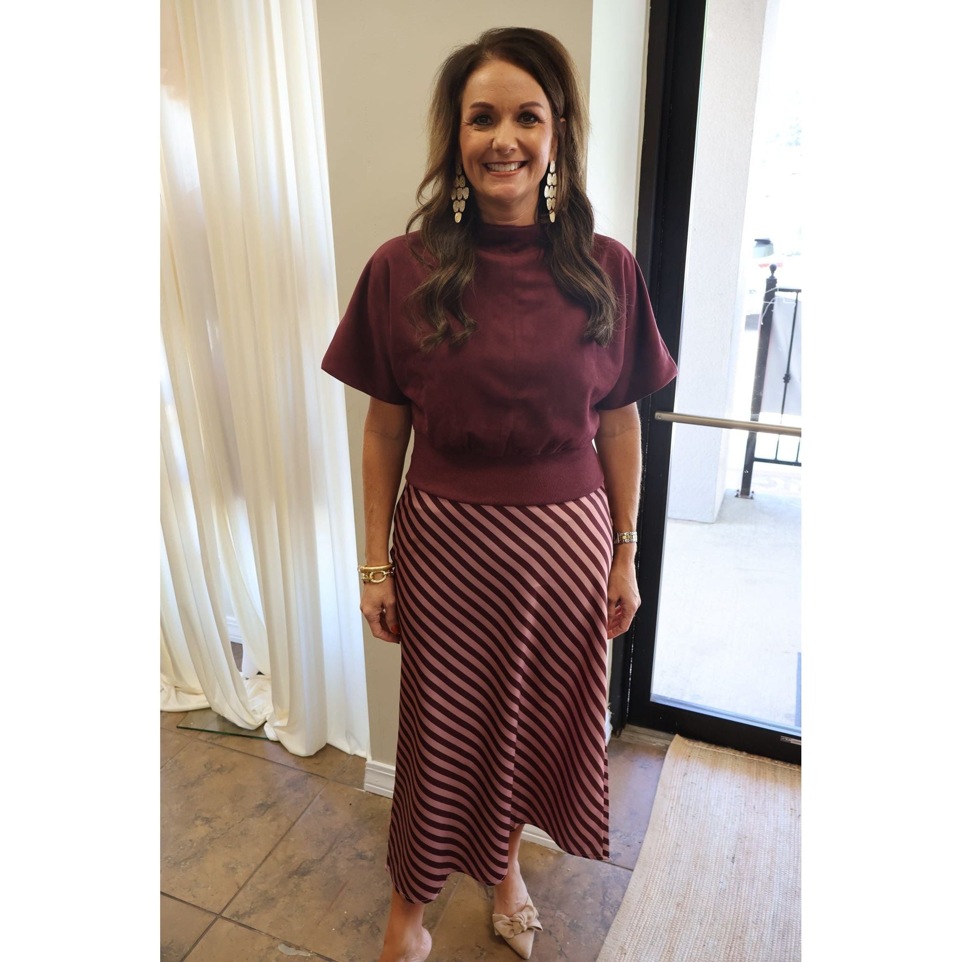 Annie Ks Boutique burgundy suede-look mock neck top worn by a smiling woman with a striped midi skirt.