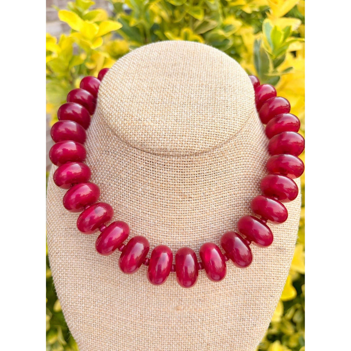 Annie Ks Boutique burgundy Rory rondelle statement necklace on a beige display bust against a yellow foliage background