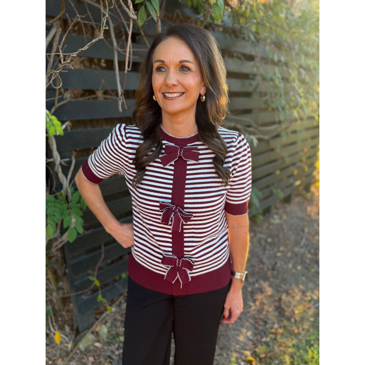 Annie Ks Boutique burgundy and white striped knit cardigan with front bow details worn by a woman outdoors