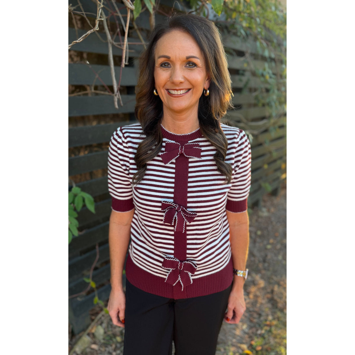 Annie Ks Boutique burgundy and white striped knit cardigan with front bow details worn by a smiling woman outdoors.