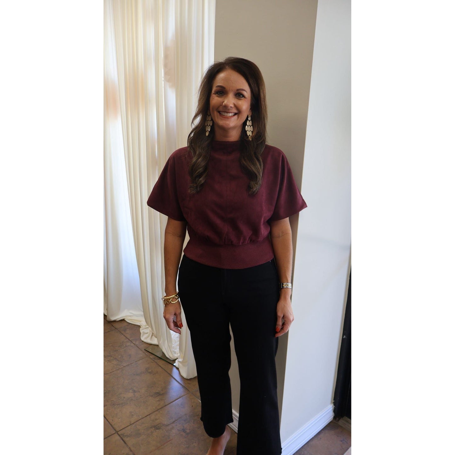 Annie Ks Boutique burgundy suede-look mock neck top with short sleeves worn by a smiling woman with gold earrings.