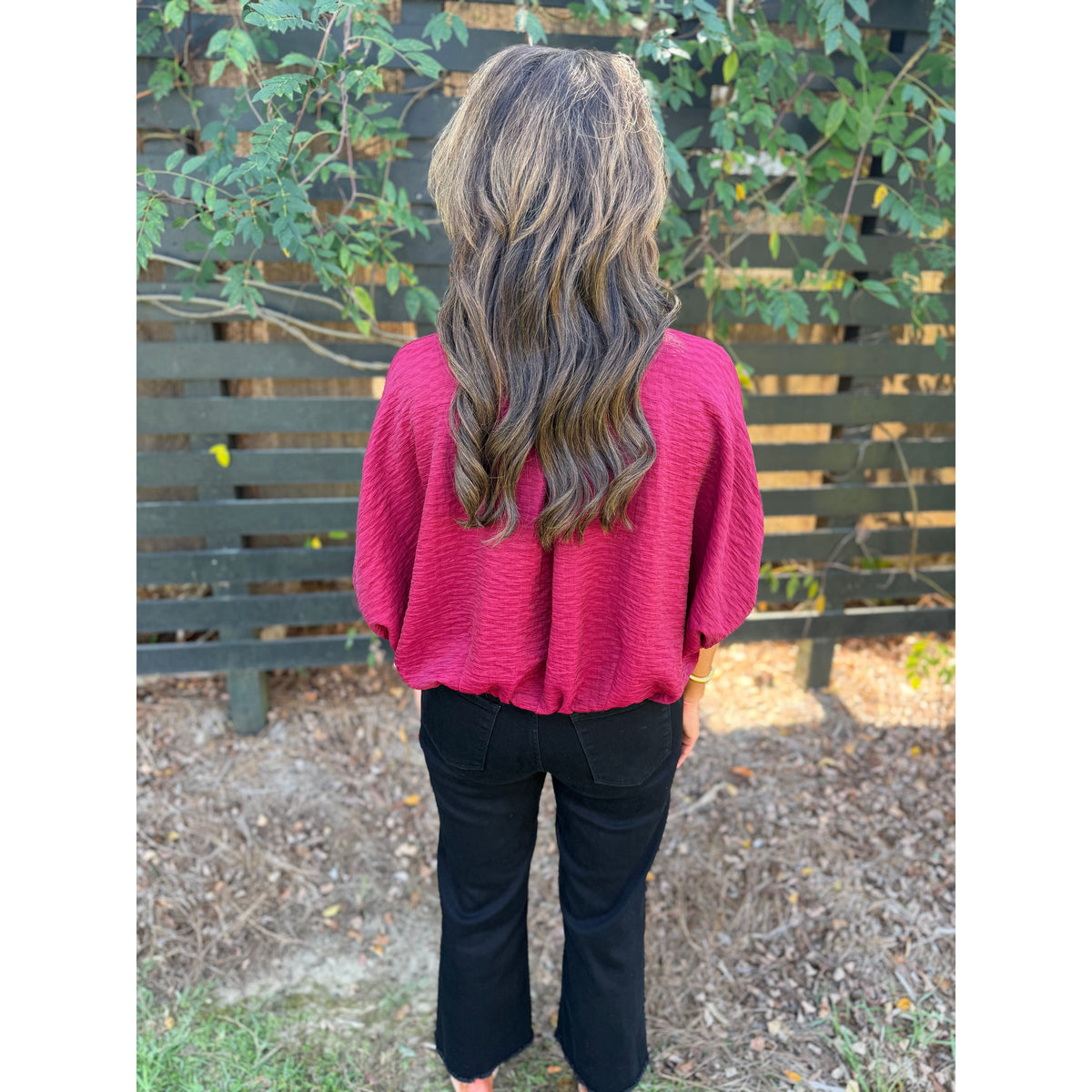 Annie Ks Boutique burgundy textured short sleeve blouse with a loose dolman fit worn with black jeans, back view