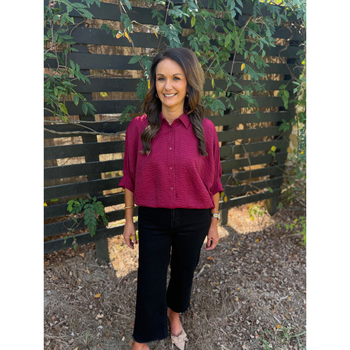 Annie Ks Boutique burgundy textured short sleeve blouse with a collar and button-front worn with black trousers.