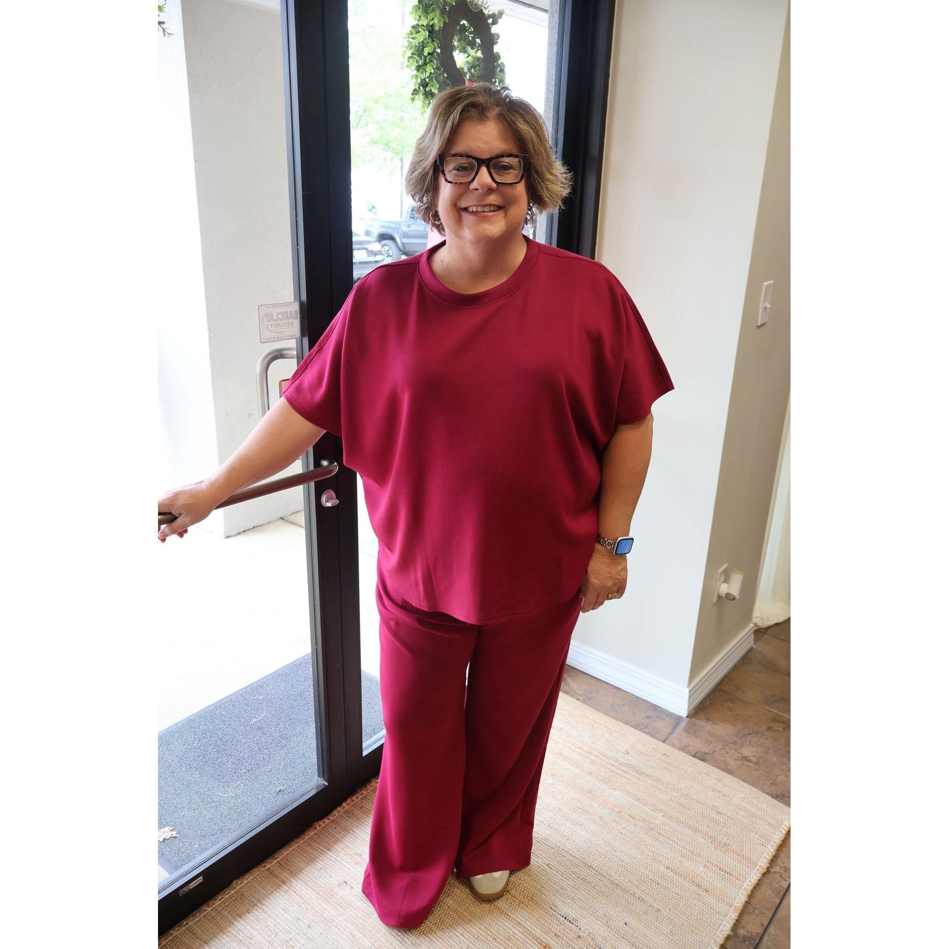 A woman wearing an Annie Ks Boutique cabernet scuba knit top and wide-leg pants set with a curved hemline.