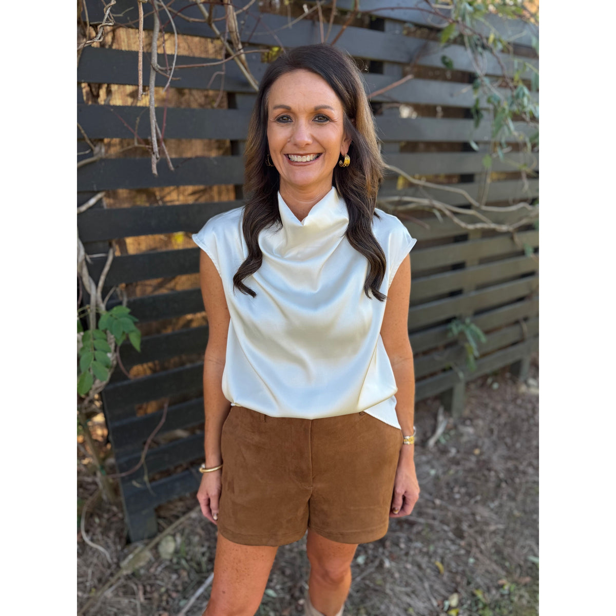 Annie Ks Boutique camel brown faux suede shorts paired with a white satin cowl neck top on a smiling woman