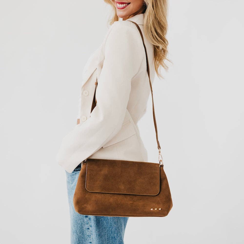 Annie Ks Boutique Miranda camel faux suede crossbody bag with adjustable strap worn by a woman in a cream blazer