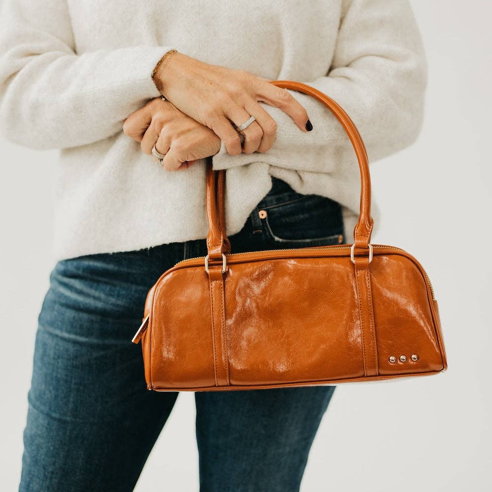Annie Ks Boutique Arlys barrel shoulder bag in caramel vegan leather held by a woman in a white sweater and jeans
